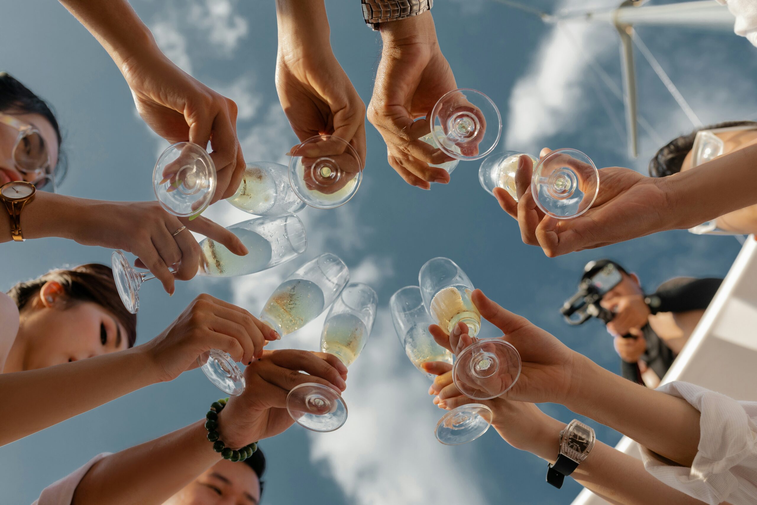 Guests at a bachelor or bachelorette party cheering with glasses of champagne on a boat with a sky background.